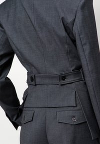Donkergrijze op maat gemaakte colbert met een aansluitend ontwerp, voorzien van een ceintuurlijn, achterzakken en knoopaccenten. Gladde textuur.