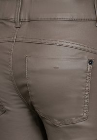 Bruna läderbyxor med en elegant design, slät yta och en bakficka med en liten logga. Synlig sömnad framhäver sömmarna.