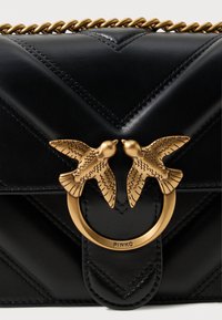 Borsa in pelle nera con cucitura a zigzag, adornata con un motivo di uccello dorato e hardware circolare. Inclusa tracolla a catena.