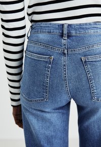 Blue denim jeans with a high waist and two back pockets, paired with a black and white striped long-sleeve shirt.