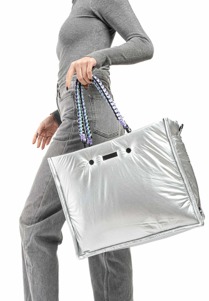 Sac fourre-tout argenté avec une texture lisse et rembourrée, présentant des accents noirs et des poignées tissées colorées pour un transport sécurisé.