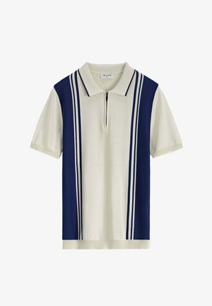 Polo à zip, corps principal couleur crème, panneaux latéraux bleu marine, et deux rayures blanches verticales le long des côtés. Texture en tricot douce.