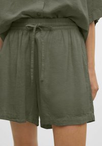 Pantaloni corti verde oliva realizzati in tessuto leggero, con una vita elastica dotata di cordino annodato e una vestibilità rilassata.