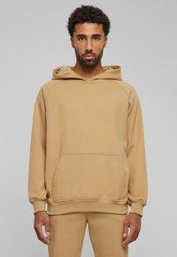 Beige hettegenser med frontlomme, snøring i hetten og ribbestrikkede mansjetter. Myk tekstur og avslappet passform. Kombinert med matchende bukser.