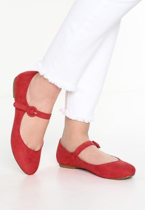 Des ballerines en daim rouge avec un bout arrondi, une sangle avec un détail de bouton, et un petit talon, associées à un jean blanc à l'ourlet effiloché.