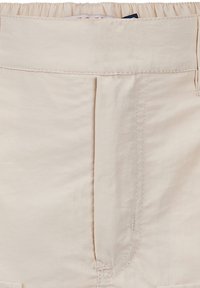 Beige shorts met een elastische tailleband, met geplooide details en gestikte accenten op de voorplooien. Zachte, gladde stoftextuur.