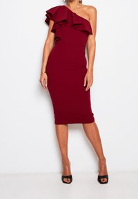 Burgunderfarbendes, figurbetontes Kleid mit einem Schulterdesign und einer strukturierten Rüsche als Akzent. Aus dehnbarem Material, knielanges Modell. Schwarze High Heels.