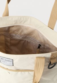 Μπεζ τσάντα tote Columbia με εσωτερική επένδυση με σχέδιο, εσωτερική τσέπη με φερμουάρ, μπεζ λουριά και ετικέτα στο μπροστινό μέρος.