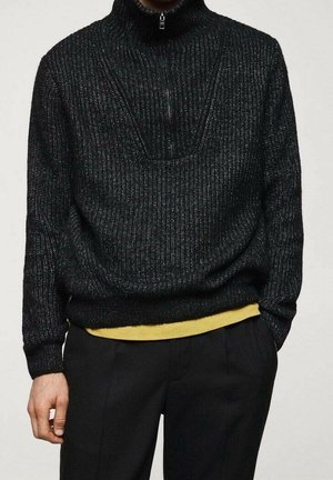 Schwarzer Strickpullover mit hohem Kragen und halbem Reißverschluss, der aus strukturiertem Material gefertigt ist und über einem gelben Hemd einen Lagenlook präsentiert.