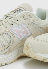 Light beige sneakers featuring mesh panels and a stitched "N" logo. The design includes textured surfaces and contrasting accents. Flat rubber outsole.