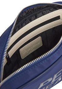 Binnenkant van een marineblauwe stoffen tas met een crèmekleurig leren ritsvak, merklabel en zwarte voering. Voorzien van een ritsluiting en een gequilt textuur.