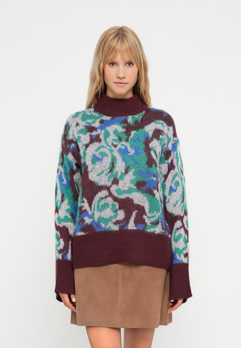 Maglione lavorato a maglia con motivo floreale in blu, verde e bordeaux. Collo alto, maniche lunghe e vestibilità rilassata, abbinato a una gonna in suede marrone.
