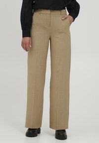 Beige weit geschnittene Hosen aus leichtem Stoff. Sie haben eine glatte Textur, Falten an der Vorderseite und seitliche Taschen.