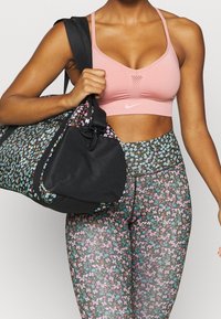 Reggiseno sportivo rosa, leggings neri con motivo floreale e accenti blu e rosa, e una borsa a tracolla nera floreale abbinata. Materiali testurizzati, spalline regolabili.