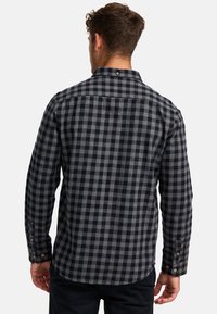 Czarna i szara koszula w kratę wykonana z miękkiego materiału flanelowego. Posiada mankiety zapinane na guziki oraz zaokrąglony dół, a także luźny kołnierzyk.