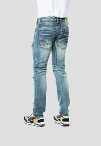 Vybledlé modré džíny s úzkým střihem, vybavené dvěma zadními kapsami a jemnými švovými detaily. Kombinovány s vícebarevnými teniskami.