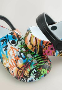 Paire de sabots colorés à motifs graffiti avec des trous de ventilation et des sangles de talon noires réglables sur un fond clair.