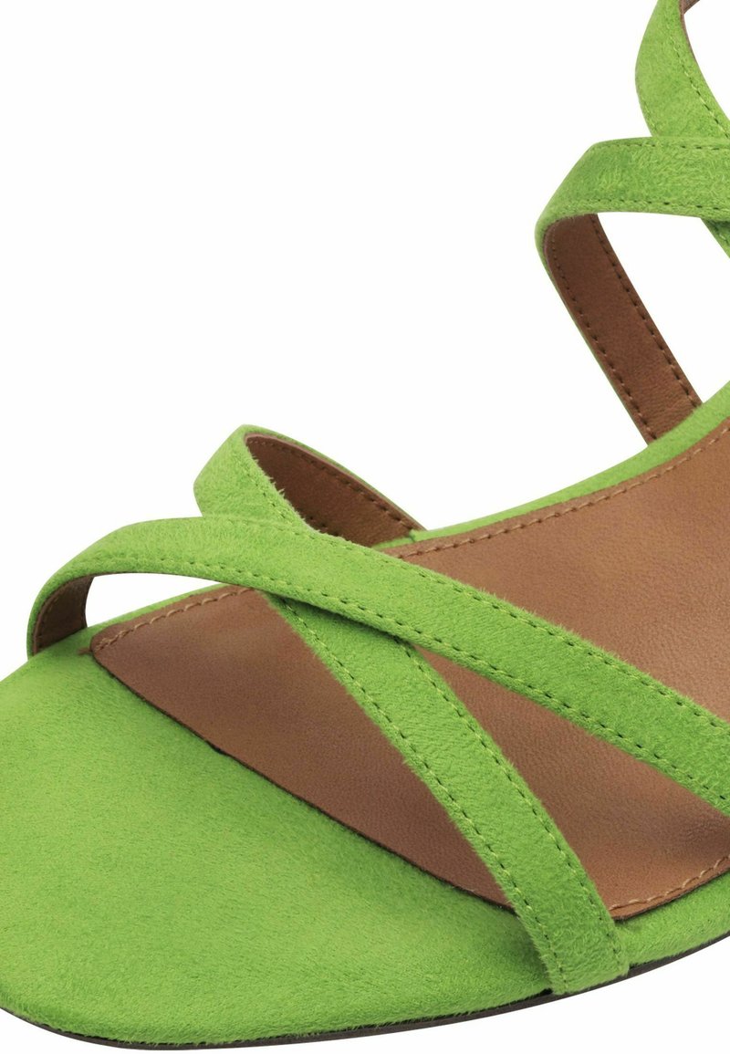 Grüne Wildledersandale mit flacher Sohle, ausgestattet mit überkreuzten Riemen und einer braunen Lederinnensohle. Einfaches Design mit glatter Textur.