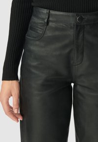 Zwarte leren broek met een gladde textuur, hoge tailleband, sluiting met een knoop aan de voorkant en zijzakken, met een getailleerde pasvorm.