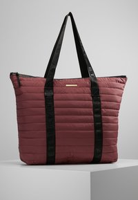 Gequilte bordeaux totebag met zwarte handvatten, ritssluiting en een gouden accentplaat. Heeft een ruime indeling en een gladde textuur.
