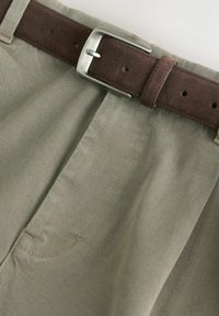 Beige Hosen mit glatter Textur, ausgestattet mit einem braunen Wildledergürtel und einer silbernen Metallschnalle. Enthält schräge Fronttaschen.