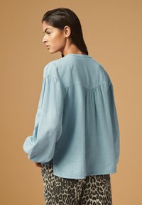  Lichtblauwe blouse met lange mouwen gemaakt van zachte stof en met een losse pasvorm, met geplooide schouderdetails. Combinatie met een opvallende broek met luipaardprint.