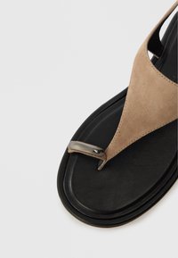 Σαμπό σε χρώμα μπεζ από σουέτ με μαύρη επίπεδη σόλα, διαθέτοντας μεταλλικό διακοσμητικό στο πόδι και λεία υφή.