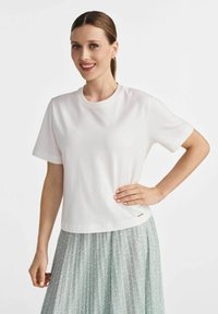Biała bawełniana koszulka z krótkim rękawem, okrągłym dekoltem i subtelnym wykończeniem dołu; zestawiona z jasnorozkładanym spódnicą z delikatnym wzorem.