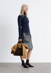 Schwarze Ledertasche mit braunen Griffen, kombiniert mit einem marineblauen Rollkragenpullover, einem metallic grauen Rock mit Krokodilprägung und einem senfgelben Pullover.