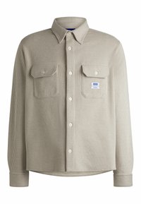 Chemise beige boutonnée en tissu côtelé, dotée de deux poches poitrine, d'un col et d'un petit label logo sur le côté gauche.
