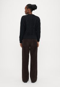 Μαύρο πουλόβερ πλεκτό με στρογγυλή λαιμόκοψη και ριμπ τελείωμα, συνδυασμένο με σκούρο καφέ παντελόνι κορδούρα με φαρδύ πόδι και πίσω τσέπες.