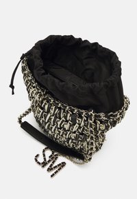 Woven handbag featuring a black and white color scheme, a drawstring closure, and a silver chain strap with a detachable accent chain.