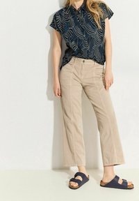 Blusa navy a maniche corte con un motivo a onde, abbinata a pantaloni beige a gamba larga. Le scarpe sono sandali navy con un dettaglio a fibbia.