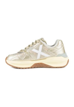 Zapatilla metálica dorada con cordones beige, logo blanco en forma de X lateral, suela cremosa gruesa y suela exterior marrón texturizada, vista desde el lateral exterior.