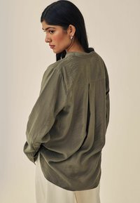 Olivenfarvet, let bluse med rund halsudskæring, lange ærmer og en center rygplissé-detalje. Tekstureret stof med bløde draperinger.