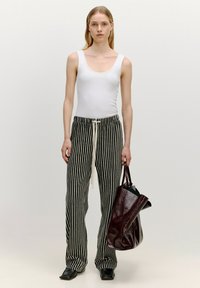 Witte mouwloze top met een ronde hals, gecombineerd met zwart en creme gestreepte broek met een koord, vastgehouden naast een glanzende donkerburgundy handtas.