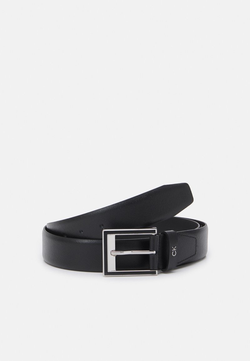 Ceinture en cuir noire avec une boucle rectangulaire argentée et le logo "ck" près de la boucle, roulée et placée sur un fond blanc.