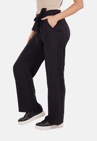 Pantaloni neri a gamba larga con vita alta, cintura in tessuto e tasche laterali, caratterizzati da una texture liscia e una silhouette rilassata.