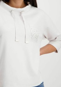 Felpa bianca con design a pullover, cordoncino regolabile, tasca frontale decorata con strass e maniche a tre quarti.