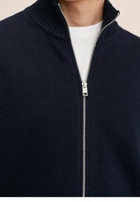 Jersey de punto azul marino con cremallera y alto cuello, que presenta una cremallera plateada y una textura acanalada en el cuello. Diseño simple y limpio.