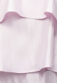 Világos rózsaszín rétegzett anyag, lágy, áramló textúrával és tisztán varrott szegélyekkel, az átfedő részek részleteivel.