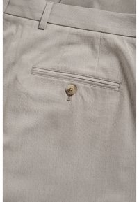 Pantalones de tela beige con un bolsillo trasero con cierre de botón y un sutil patrón de tejido texturizado. Diseño entallado con trabillas para cinturón.
