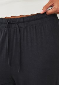 Zwarte joggingbroek met een zachte, rekbare stof en een elastische tailleband. Het materiaal lijkt glad en is geschikt voor casual gebruik.