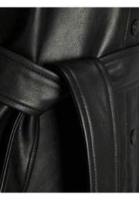 Mustan nahkavyön teksturoidulla pinnalla, jossa on solmittu muotoilu ja sileä, taitettu päällys. Huomaamaton ommel näkyvissä.