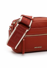 Red textured leather crossbody bag with a woven strap and adjustable hardware, featuring a front zip pocket and logo detail.