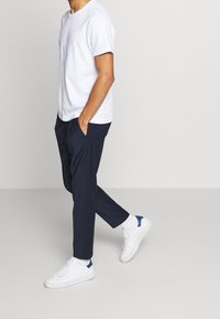 Witte katoenen t-shirt, marineblauwe broek, witte sneakers met blauwe accenten. Casual fit, korte mouwen, zak aan de zijkant van de broek.