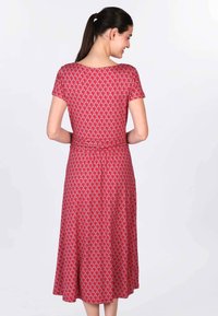 Rotes knielanges Kleid mit kurzen Ärmeln, das ein sich wiederholendes geometrisches Muster aufweist und eine taillierte Passform hat, aus einem weichen, leichten Stoff gefertigt.
