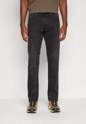 Jeans de algodón negros con corte slim, diseño de cinco bolsillos y un ligero desvanecimiento. Combinados con zapatillas deportivas negras y amarillas.