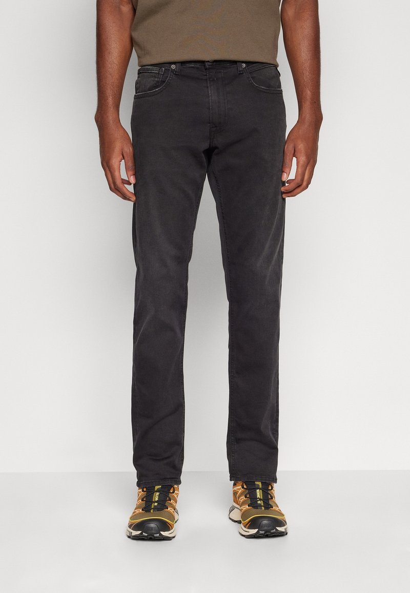 Jeans de algodón negros con corte slim, diseño de cinco bolsillos y un ligero desvanecimiento. Combinados con zapatillas deportivas negras y amarillas.