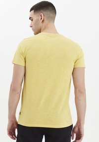 Gul bomulds t-shirt med rund hals og korte ærmer. Har en subtil tekstur og et lille logo accent på sidekanten.
